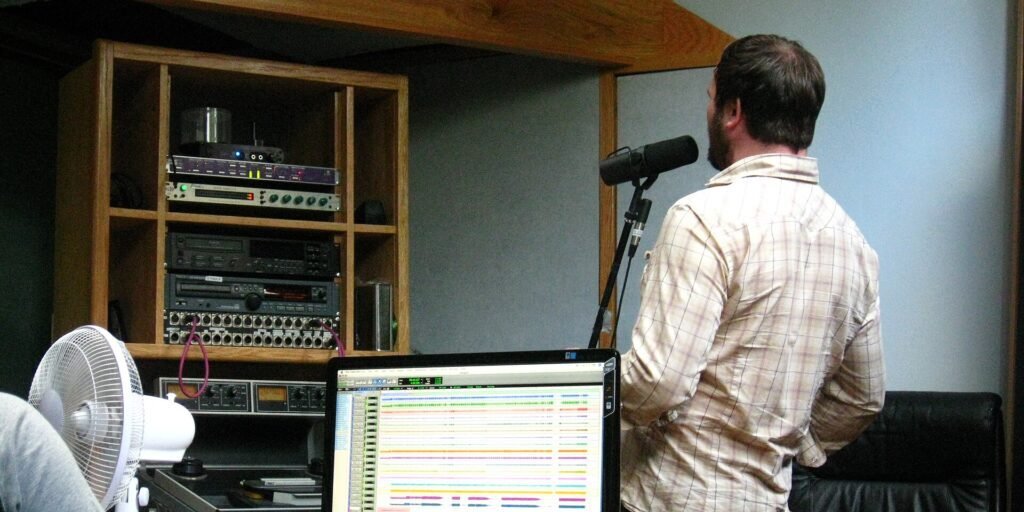 Voice actor recording dialogue into a microphone at a vocal dubbing booth with audio interface displayed on monitor