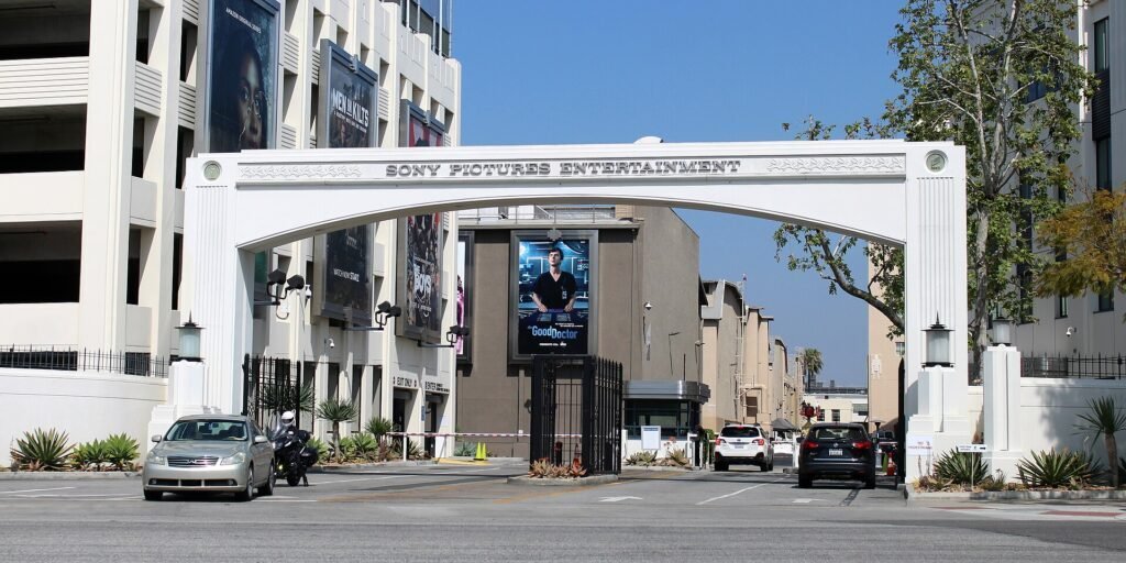 White arched studio gate reading Sony Pictures Entertainment, with parked cars and billboards along the street