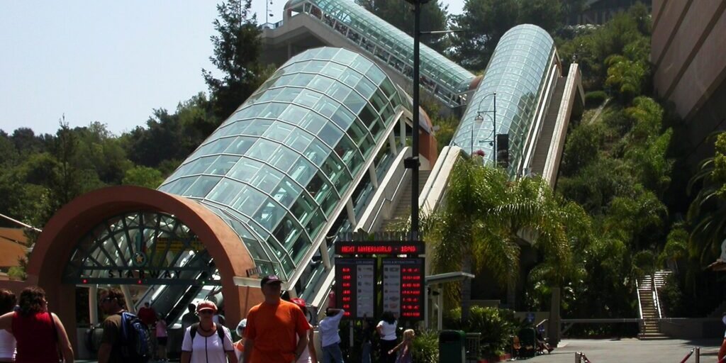 Glass-enclosed escalators climbing a hillside at Universal Studios Hollywood, with visitors walking in the foreground