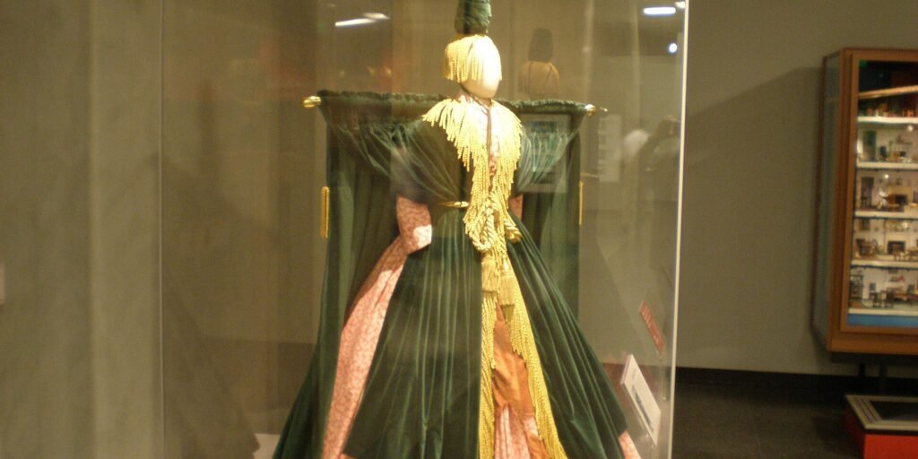 A dramatic green and gold gown displayed in a museum case