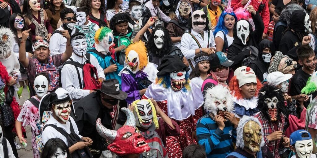 Crowd of paradegoers wearing elaborate masks, including skulls, devils and ghoulish faces